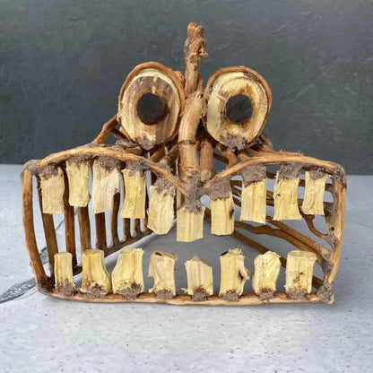 Handcrafted wooden mask with large eye sockets and toothy grin.