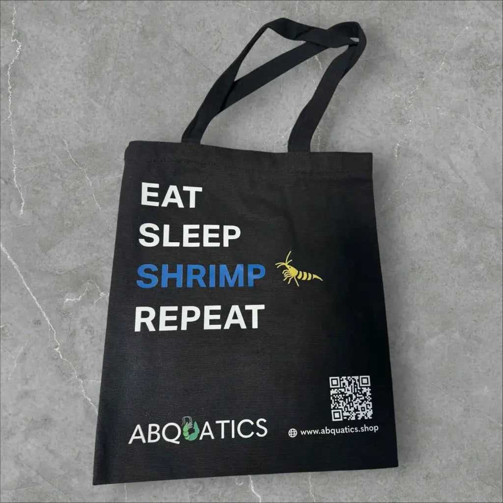 Black fabric tote bag with a white and blue ’EAT SLEEP SHRIMP REPEAT’ design and a yellow shrimp graphic.